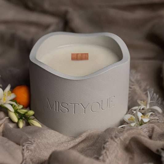 Mistyque candle in light grey concrete pot with wooden wick, styled with white florals and citrus — The Scent of Silence standard candle